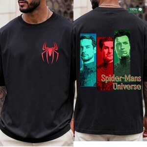 May include: A black short-sleeved t-shirt featuring a red spider logo on the front chest. The back displays three rectangular portraits of different characters in teal, red, and green, with the text Spider-Mans Universe printed below.