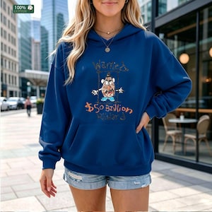 Op de afbeelding: Een marineblauwe hoodie met een voorzak en een capuchon met trekkoord. De hoodie heeft een cartoonafbeelding van een aardappelkop met de woorden "Wanted" en "$50 Billion" in handschrift. De linkerbovenhoek heeft een label "100% Katoen".