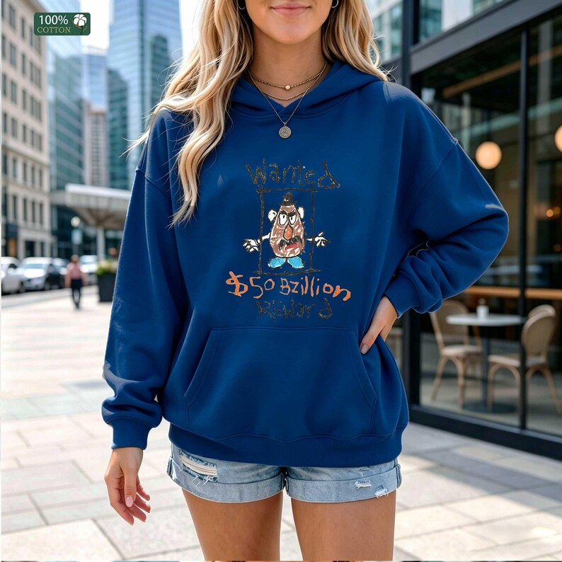 Op de afbeelding: Een marineblauwe hoodie met een voorzak en een capuchon met trekkoord. De hoodie heeft een cartoonafbeelding van een aardappelkop met de woorden "Wanted" en "$50 Billion" in handschrift. De linkerbovenhoek heeft een label "100% Katoen".