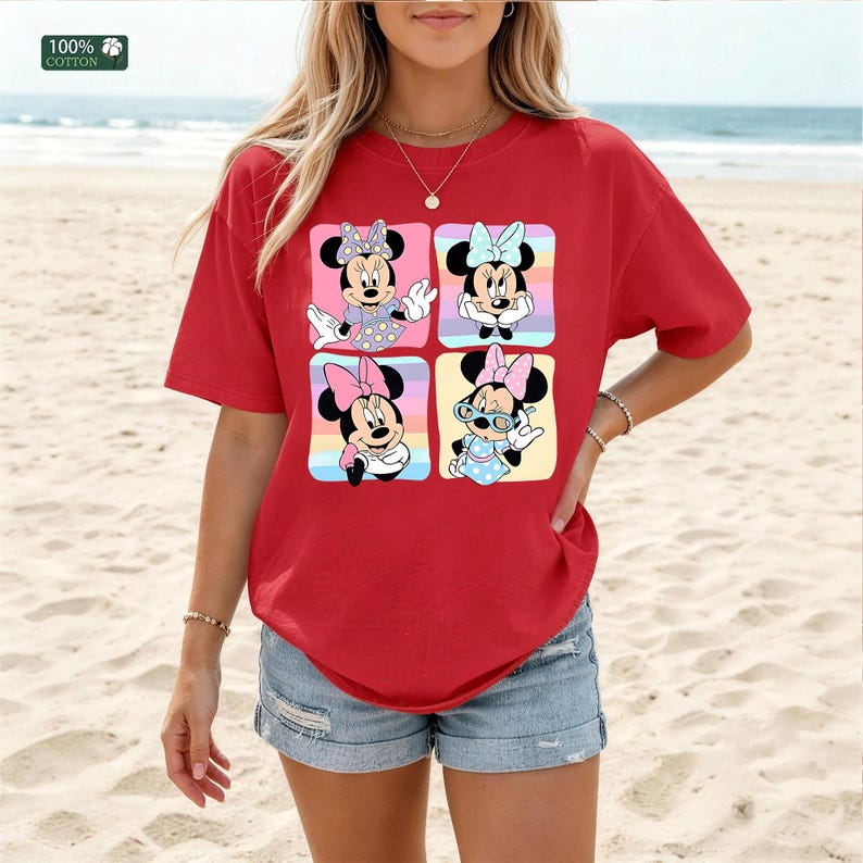 May include: A red short-sleeved t-shirt featuring a graphic print of four squares, each containing a different illustration of Minnie Mouse in various outfits and poses. The shirt is made of 100% cotton and has a crew neckline. The graphic includes pastel colors.