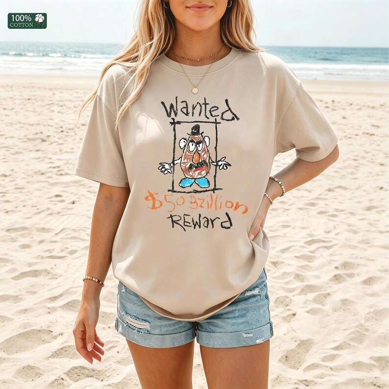 Op de afbeelding: Beige T-shirt met korte mouwen met een cartoonillustratie van een aardappelpersonage in een gezocht poster. De tekst "Wanted" en "$50,3 miljard Reward" staan boven en onder het personage. Het shirt is gemaakt van 100% katoen.