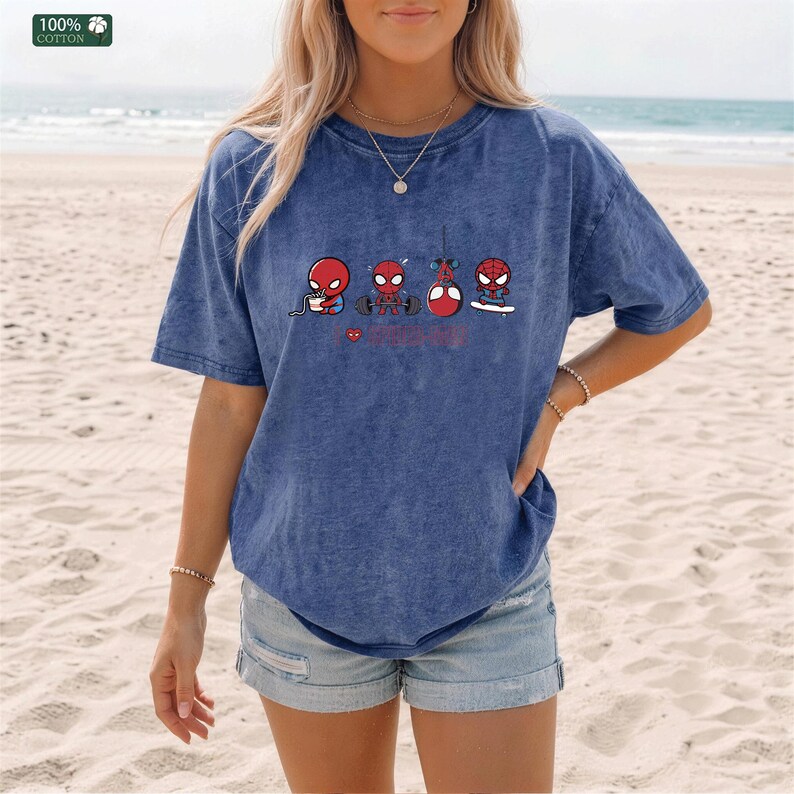 May include: A blue acid-wash t-shirt featuring a graphic print of four cartoon Spider-Man characters performing various activities including eating, lifting weights, hanging from a web, and skateboarding, with a small red heart icon.