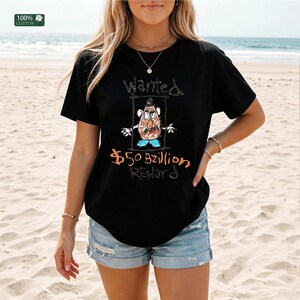Op de afbeelding: Zwart T-shirt met een handgetekende afbeelding van een aardappelpersonage in een gezocht poster. De tekst op het shirt luidt "Wanted" boven het personage en "$50 Bzillion REWARD" eronder. Het shirt is gemaakt van 100% katoen.