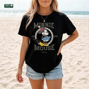 May include: Black t-shirt featuring a graphic of Minnie Mouse in a checkered circle, with the text "MINNIE MOUSE 1928 Disney". The shirt is made of 100% cotton.