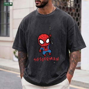 Op de afbeelding: Donkergrijs T-shirt met een cartoon Spider-Man afbeelding. Het ontwerp bevat een rood en blauw Spider-Man karakter dat aan een web hangt, met het woord "SPIDERMAN" in het rood. Het shirt is gemaakt van 100% katoen.