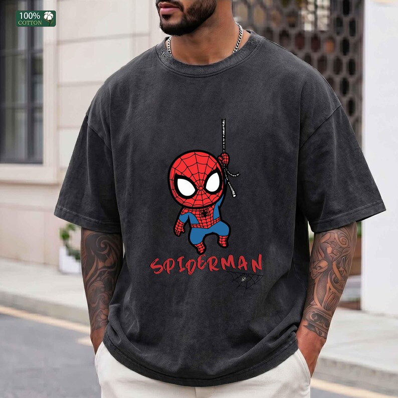Op de afbeelding: Donkergrijs T-shirt met een cartoon Spider-Man afbeelding. Het ontwerp bevat een rood en blauw Spider-Man karakter dat aan een web hangt, met het woord "SPIDERMAN" in het rood. Het shirt is gemaakt van 100% katoen.