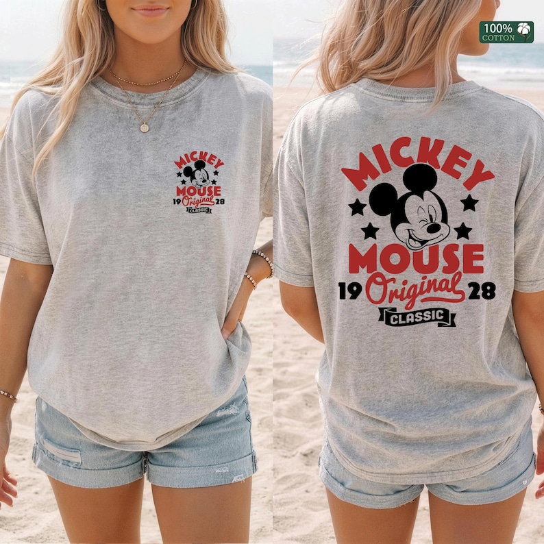 May include: A light gray t-shirt featuring a Mickey Mouse graphic on the front and back. The design includes Mickey's face, the words "Mickey Mouse," "Original 28," and "Classic" in red and black.