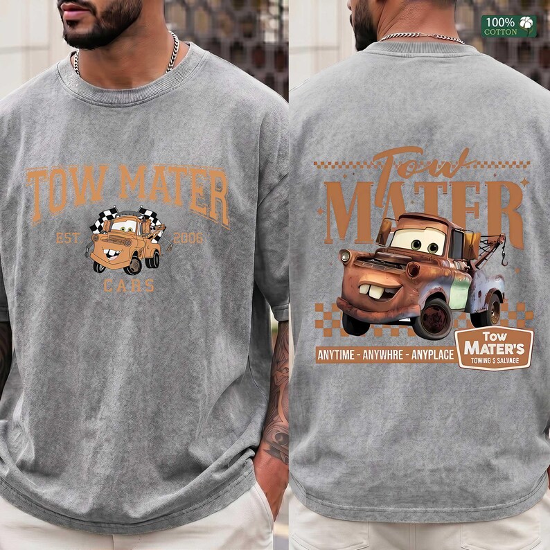 May include: A grey acid-wash t-shirt featuring a graphic of the character Tow Mater. The front displays the text Tow Mater Est 2006. The back features a larger graphic of the character with the text Tow Mater, Anytime, Anywhre, Anyplace.