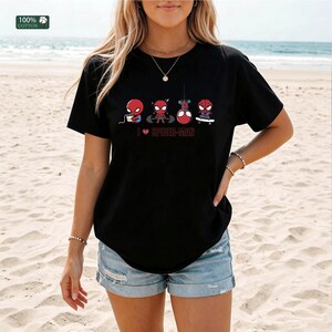 May include: A black short-sleeve t-shirt featuring a graphic of four small Spider-Man figures performing different activities, including eating, lifting weights, hanging, and skateboarding, with the text I heart SPIDER-MAN printed below.