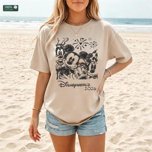 Puede incluir: Camiseta beige con un gr&aacute;fico negro con los personajes de Disney Mickey Mouse, Minnie Mouse, Donald Duck, Goofy y Pluto. El texto "Disneyworld 2020" est&aacute; debajo. La camiseta es 100% algod&oacute;n.