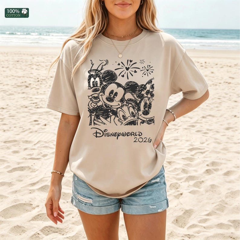 Puede incluir: Camiseta beige con un gr&aacute;fico negro con los personajes de Disney Mickey Mouse, Minnie Mouse, Donald Duck, Goofy y Pluto. El texto "Disneyworld 2020" est&aacute; debajo. La camiseta es 100% algod&oacute;n.
