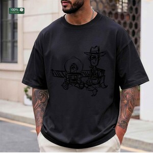 May include: A black short-sleeved t-shirt featuring a dark, sketch-style graphic print of two animated characters, a space ranger and a cowboy, centered on the chest. The garment is made of 100% cotton and has a crew neckline with a relaxed fit.