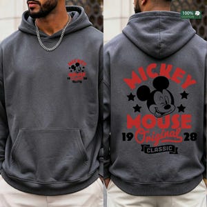 May include: Charcoal gray hoodie featuring a front and back design of Mickey Mouse. The front has a small graphic, while the back displays a larger Mickey Mouse graphic with the text "Mickey Mouse Original Classic 1928". Made of 100% cotton.