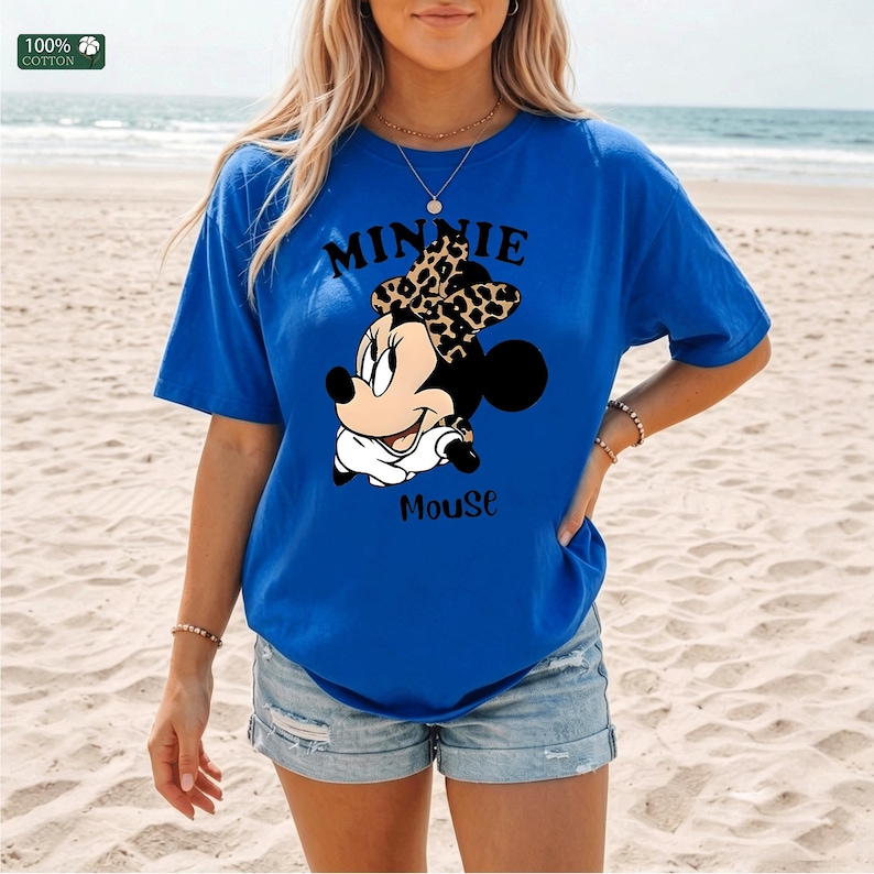 May include: Royal blue t-shirt featuring a Minnie Mouse graphic. The graphic includes the text "MINNIE Mouse" with Minnie wearing a leopard print bow. The shirt is made of 100% cotton.