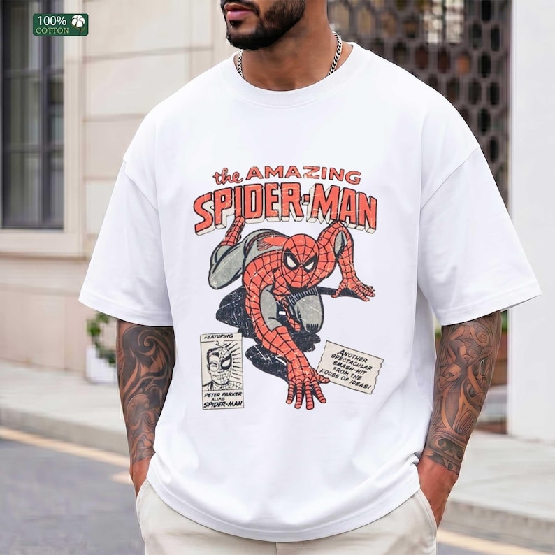 May include: A white short-sleeved t-shirt featuring a vintage-style graphic of Spider-Man in a crouching pose. The text reads The Amazing Spider-Man, Peter Parker Alias Spider-Man, and Another Spectacular Smash-Hit From The House Of Ideas.