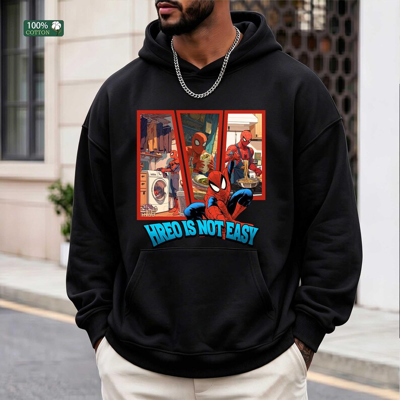 May include: A black hooded sweatshirt featuring a graphic print of Spider-Man performing household chores like laundry and cooking. Below the illustration, the text reads HREO IS NOT EASY in bold blue letters. The garment includes a front kangaroo pocket.