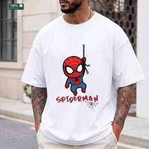 Op de afbeelding: Wit T-shirt met een cartoon Spider-Man ontwerp in rood en blauw, met het woord "SPIDERMAN" in rood script eronder. Er is ook een kleine spinnenwebafbeelding aanwezig. Het shirt is gemaakt van 100% katoen.