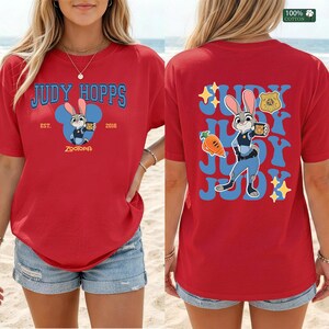 Pu&ograve; includere: Una t-shirt rossa con una grafica di Judy Hopps di Zootropolis. Il davanti mostra il testo Judy Hopps, Est. 2016, e un'icona del personaggio. Il retro mostra una grande illustrazione di Judy Hopps, una carota, un distintivo e il nome Judy.