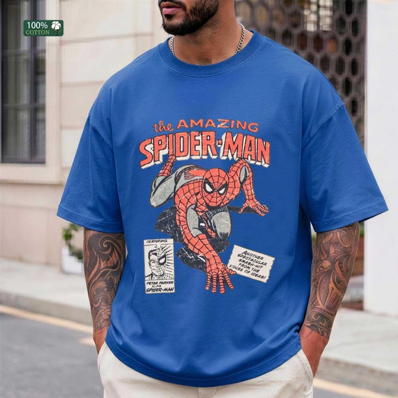 May include: A blue short-sleeve t-shirt featuring a vintage-style graphic of Spider-Man in a crouching pose. The design includes the text "the AMAZING SPIDER-MAN" in orange and white, along with a small comic book panel and a text box.