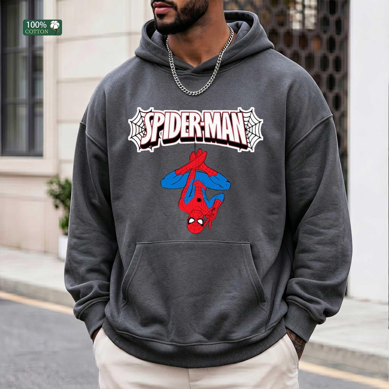 May include: A charcoal grey hoodie with a Spider-Man graphic. The graphic shows Spider-Man hanging upside down, with the word "SPIDER-MAN" in a white webbed design. The hoodie has a front pocket and a drawstring hood. The tag reads "100% cotton."