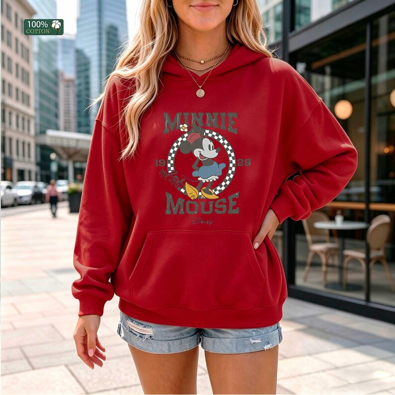 May include: A red hooded sweatshirt featuring a graphic of Minnie Mouse in a checkered circle, with the text "MINNIE MOUSE 1926". The sweatshirt has a front pocket and a drawstring hood. The upper left corner has a "100% cotton" tag.