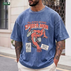 May include: A blue acid-wash t-shirt featuring a vintage-style graphic of Spider-Man in a crouching pose. The text reads "the AMAZING SPIDER-MAN" in orange, with a small comic book panel insert and a white box containing text about the character.