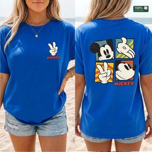 May include: Royal blue t-shirt featuring a Mickey Mouse peace sign graphic on the front and a four-panel design on the back. The back design includes Mickey's face, hands, and the word "Mickey" in red.