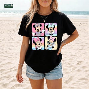May include: A black short-sleeve t-shirt featuring a graphic print of four squares, each containing a different illustration of Minnie Mouse in various poses and outfits. The top left corner includes a small green square with 100% COTTON text.