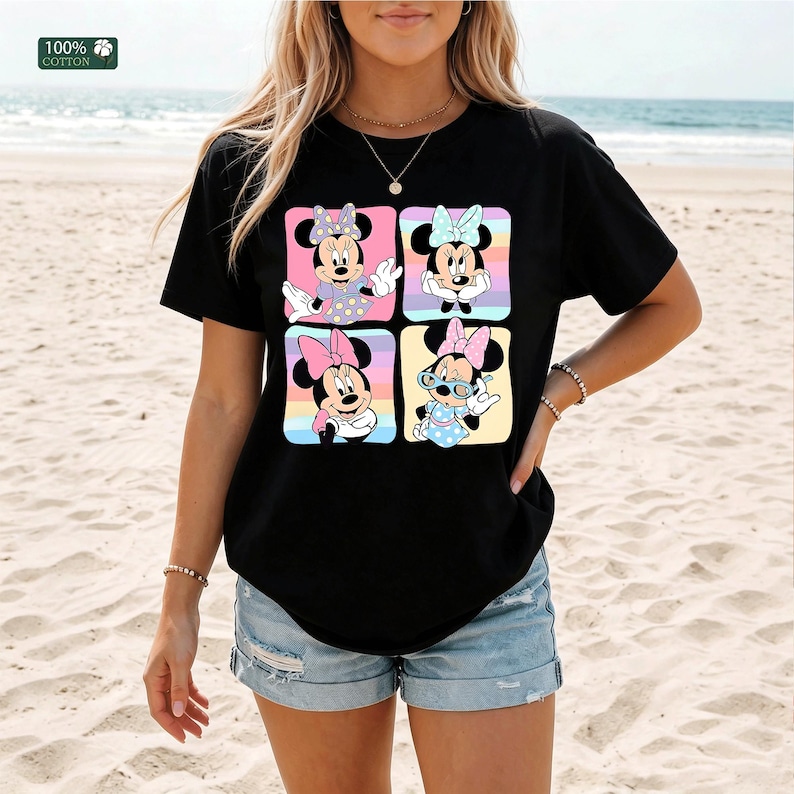 May include: A black short-sleeve t-shirt featuring a graphic print of four squares, each containing a different illustration of Minnie Mouse in various poses and outfits. The top left corner includes a small green square with 100% COTTON text.