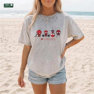 May include: A light gray short-sleeve t-shirt featuring a graphic of four small Spider-Man characters performing different activities, including eating, lifting weights, hanging, and skateboarding, with the text I heart SPIDER-MAN below.