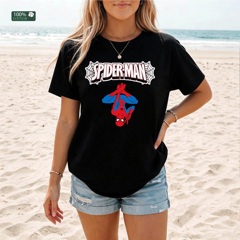 May include: Black t-shirt with the Spider-Man logo and a graphic of Spider-Man in a red and blue suit. The text "SPIDER-MAN" is in white, outlined in black, and set against a white web design. The shirt is made of 100% cotton.