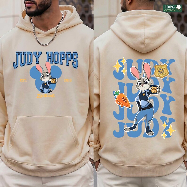 Pu&ograve; includere: Una felpa con cappuccio beige che presenta una grafica di Judy Hopps sul davanti con il testo JUDY HOPPS EST. 2016. Il retro mostra una grafica pi&ugrave; grande di Judy Hopps, una carota, un distintivo della polizia e stelle con il testo JUDY.