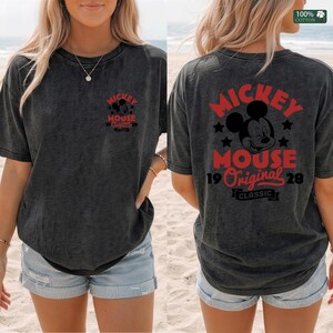 May include: Dark gray t-shirt featuring the text "Mickey Mouse 19 Original 28" in red on the front and back. The back of the shirt also displays a Mickey Mouse graphic and the word "Classic". The shirt is made of 100% cotton.