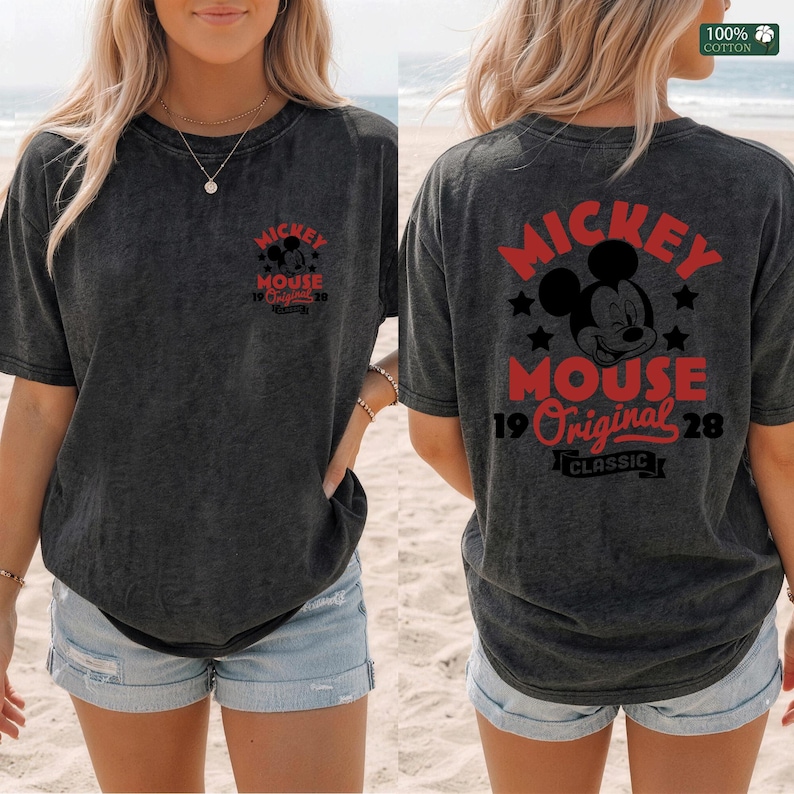 May include: Dark gray t-shirt featuring the text "Mickey Mouse 19 Original 28" in red on the front and back. The back of the shirt also displays a Mickey Mouse graphic and the word "Classic". The shirt is made of 100% cotton.