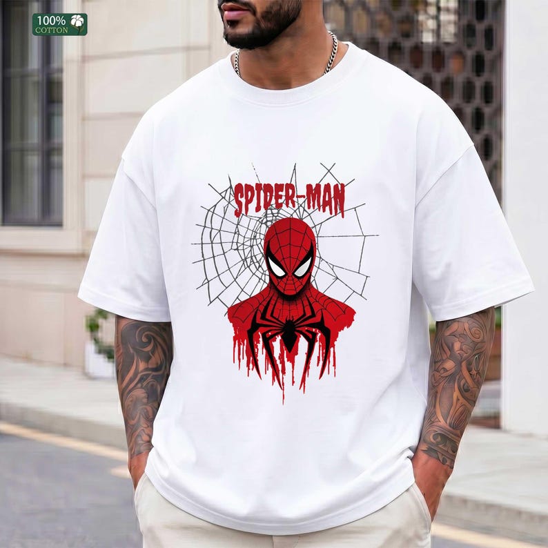 May include: White t-shirt featuring a red and black Spider-Man graphic. The design includes the words "SPIDER-MAN" in red above the character's head, with a spider web background. The shirt is made of 100% cotton.