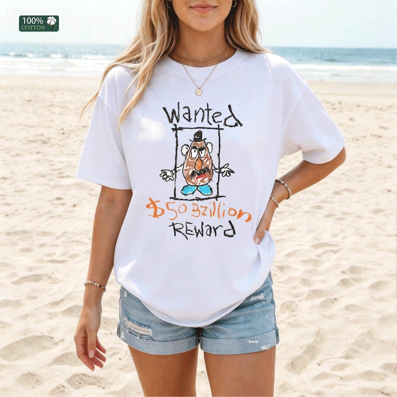 Op de afbeelding: Wit T-shirt met een handgetekende afbeelding van een aardappelachtig personage in een gezocht poster. De tekst "Wanted" staat boven het personage en "$50 Billion Reward" eronder. Het shirt is gemaakt van 100% katoen.