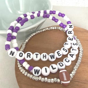 May include: A set of three beaded bracelets. One features purple and white round beads. Another features white round beads with black letters spelling NORTHWESTERN WILDCATS. The third is made of metallic silver beads with a brown football charm.