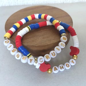 May include: Two colorful bracelets with the words "DISNEY CRUISE AHOY" spelled out in white beads with gold lettering. One bracelet has red, white, blue, and yellow beads. The other has a red Mickey Mouse head charm.