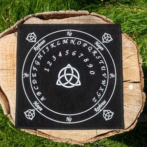 May include: Black Ouija board with white lettering and symbols. The board features the alphabet, numbers, and the words "Yes," "No," "Maybe," and "Rephrase." A central Celtic knot design is visible.