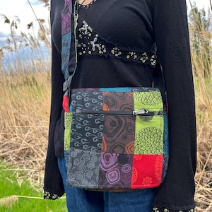 May include: A colourful patchwork crossbody bag. The bag features a variety of patterns and colours, including red, green, blue, and purple. It has a black zip and a matching strap.