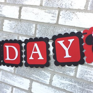 May include: A birthday banner with red and black scalloped edges. The banner spells out "BIRTHDAY" in white letters on red squares. A Minnie Mouse head with a pink polka dot bow is at the end of the banner.