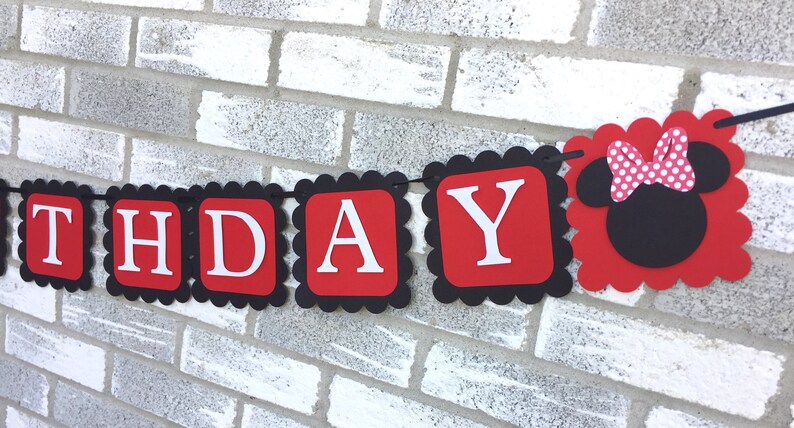 May include: A birthday banner with red and black scalloped edges. The banner spells out "BIRTHDAY" in white letters on red squares. A Minnie Mouse head with a pink polka dot bow is at the end of the banner.