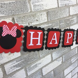 May include: A red and black banner spelling "HAPPY" in white letters. The banner features a Minnie Mouse head with a polka dot bow. The banner has a scalloped edge and is strung on a black string, suitable for a party.