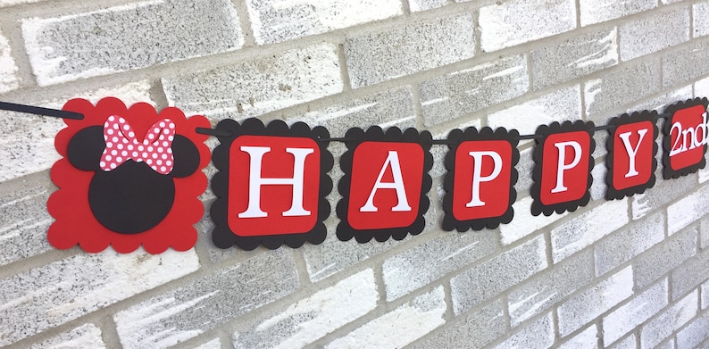 May include: A celebratory banner with red and black scalloped edges. The banner reads "HAPPY 2nd" in white letters on red squares. A Minnie Mouse head with a polka dot bow is on the left.