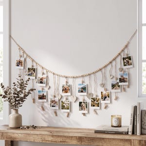 May include: A wall-mounted photo display garland featuring a long string of light-colored wooden beads. Multiple small square photographs are suspended from the garland by thin twine and wooden clips, interspersed with small wooden heart cutouts.