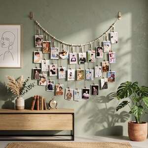 May include: A wall-mounted photo display featuring a string of light-colored wooden beads draped in a curve. Numerous small rectangular photographs are suspended from the beads by thin strings and wooden clips, creating a layered collage effect.