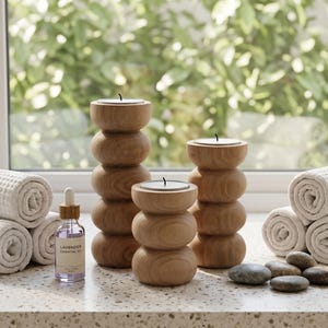 Op de afbeelding: Een spa-thema display met drie houten kandelaars, opgerolde witte handdoeken en een flesje lavendel etherische olie. De kandelaars zijn gestapeld met afgeronde secties. Gladde stenen zijn gerangschikt in de buurt van de kaarsen.