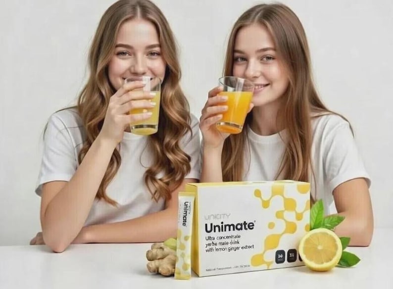 K&ouml;nnte beinhalten: Eine Packung Unimate Yerba-Mate-Getr&auml;nkekonzentrat mit Zitronen-Ingwer-Extrakt, ein einzelner Portionsbeutel, eine frische Ingwerwurzel und eine aufgeschnittene Zitrone. Zwei Gl&auml;ser mit gelber Fl&uuml;ssigkeit stehen hinter der Produktverpackung.