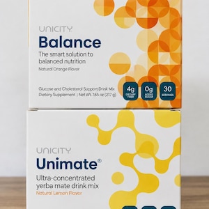 K&ouml;nnte beinhalten: Zwei gestapelte rechteckige Schachteln mit Unicity Nahrungserg&auml;nzungsmitteln. Die obere Schachtel ist Balance, ein Getr&auml;nkepulver mit nat&uuml;rlichem Orangengeschmack, Nettogewicht 217 g. Die untere Schachtel ist Unimate, ein hochkonzentriertes Yerba-Mate-Getr&auml;nkepulver mit nat&uuml;rlichem Zitronengeschmack, Nettogewicht 153 g. Beide Schachteln enthalten 30 Portionen.