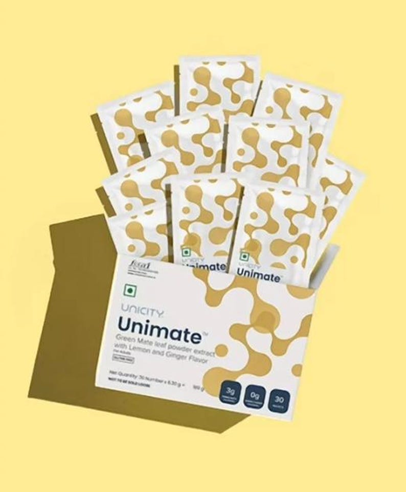 K&ouml;nnte beinhalten: Eine wei&szlig;e Schachtel und mehrere einzelne P&auml;ckchen mit Unicity Unimate Gr&uuml;nem Mate-Blatt-Pulverextrakt mit Zitronen- und Ingwergeschmack. Die Verpackung zeigt ein goldenes abstraktes Muster, den Text Unimate und 30 P&auml;ckchen &agrave; 6,30g.